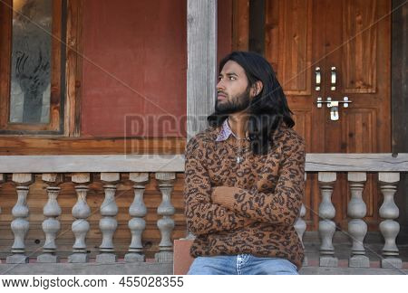 Front View A Good Looking Long Haired Young Guy Looking Sideways While Sitting In Old Temple Posing 