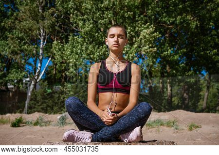 Young Woman Dressed In Sportswear Sits On Beach For Learning Music Listening For Training In Headpho