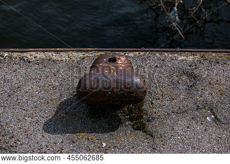 A Very Old, Rusty Iron Bollard On A Concrete Pier By The River. Pier At The Old River Station. Close