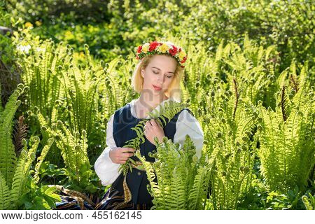 Young Woman In National Clothes And Wreath Against The Background Of A Green Fern. Ligo Latvian Holi