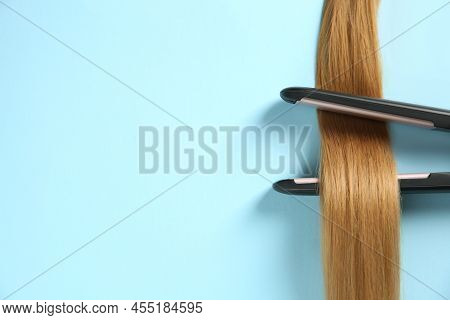 Modern Straightener With Blonde Hair Lock On Light Blue Background, Top View. Space For Text