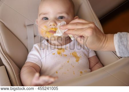 Mother Wiping Baby Using Wet Wipes After A Meal, Introducing First Solid Food Meal, Baby Sitting In 