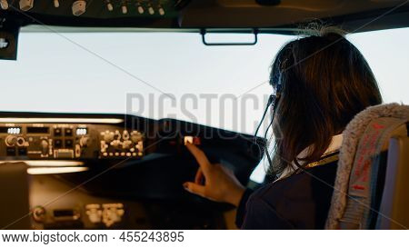 Woman Copilot In Uniform Preparing To Takeoff For Airline Flight, Pushing Buttons On Dashboard And C