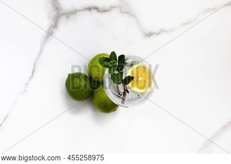 A Glass Of Water, Lemon And Mint And Lime On A White Table For Healthy Life, Energy, Thermoregulatio