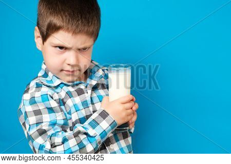 A 4-year-old Boy Holds A Glass Of Milk And Squirms Looking Into The Camera. Cows Milk Protein Allerg