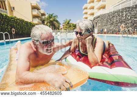 Happy Old Senior Caucasian Couple Enjoy The Summer Leisure Activity Swimming At The Pool With Colour