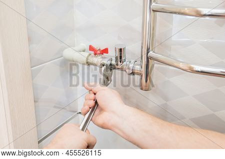 A Male Plumber Repairs The Pipes Of The Heated Towel Rail In The Bathroom.