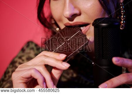 Young Caucasian Woman Sitting In Studio In Pink Neon Light Recording Chocolate Bar Biting Sounds For