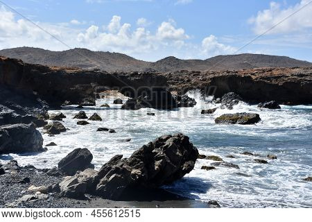 Beautiful Black Stone Beach With Lava Rock And Waves Crashing Ashore.