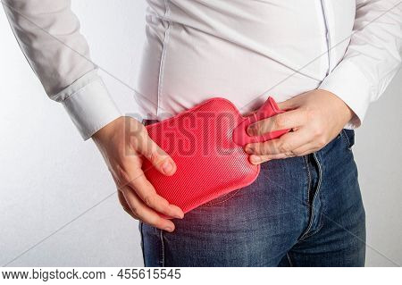 A Man Applies A Red Heating Pad With Hot Water To His Hip Joint. Treatment Of Arthritis And Inflamma