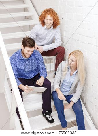 business, technology and startup concept - smiling creative team with tablet pc computer sitting on staircase