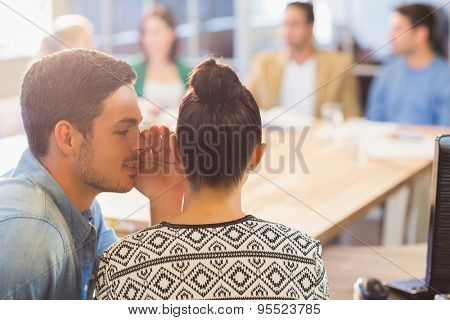 Casual businessman whispering secret to his colleague in the office