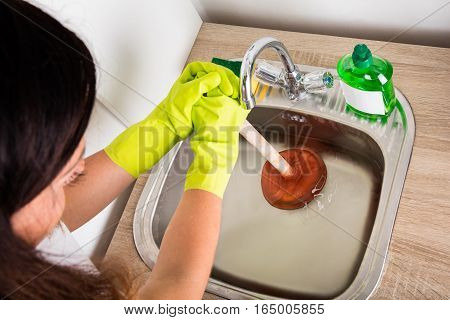 Close-up Of Person Using Plunger In The Kitchen Sink