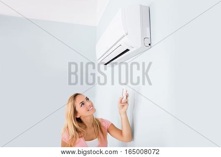 Portrait Of A Happy Woman Holding Remote Control In Front Of Air Conditioner At Home