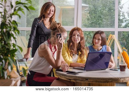 Group of four pretty businesswomen working togeather with new startup project using laptop computer in modern loft. People and teamwork concept - happy creative team in office. Casually dressed female colleagues talking in a meeting room.