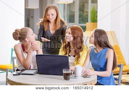 Group of four pretty businesswomen working togeather with new startup project using laptop computer in modern loft. People and teamwork concept - happy creative team in office. Casually dressed female colleagues talking in a meeting room.