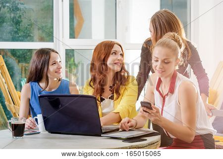 Group of four pretty businesswomen working togeather with new startup project using laptop computer in modern loft. People and teamwork concept - happy creative team in office. Casually dressed female colleagues talking in a meeting room.
