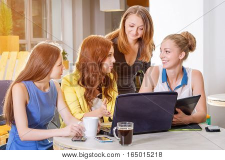 Group of four pretty businesswomen working togeather with new startup project using laptop computer in modern loft. People and teamwork concept - happy creative team in office. Casually dressed female colleagues talking in a meeting room.