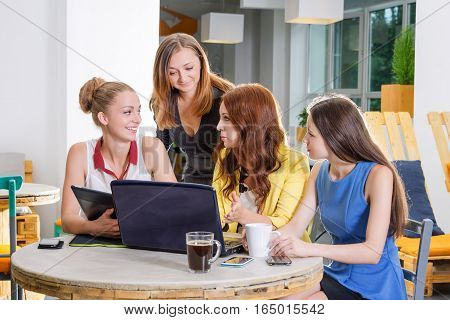 Group of four pretty businesswomen working togeather with new startup project using laptop computer in modern loft. People and teamwork concept - happy creative team in office. Casually dressed female colleagues talking in a meeting room.