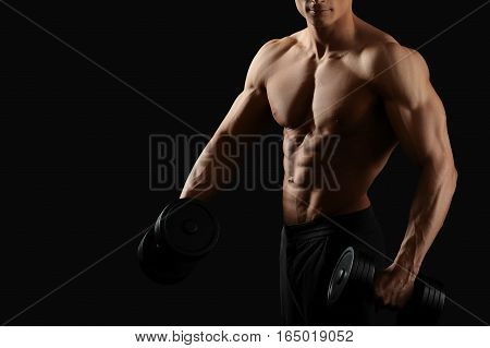 Fitness routine. Cropped horizontal shot of a young fit bodybuilder exercising with dumbbells posing shirtless on black background