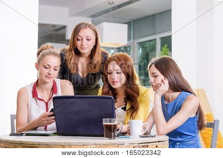 Group of four pretty businesswomen working togeather with new startup project using laptop computer in modern loft. People and teamwork concept - happy creative team in office. Casually dressed female colleagues talking in a meeting room.