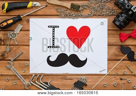 Father's Day flat lay mock up template with hand lettering greeting note and male accessories: tools, chain, photo camera, bow tie and funny photo booth paper mustache