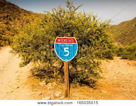Quriky idea of a California interstate 5 traffic sign in front of desert thorn tree with gravel road fork in South Africa