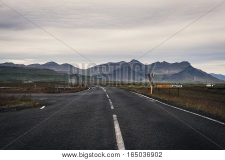 Iceland Road With Mountains On The Horizon. Empty Road In Rural Icelandic Landscape With Road Sign T