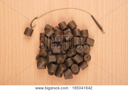 Fishing bait with hook and brown pre-drilled halibut pellets for carp fishing isolated on wood background with soft shadow