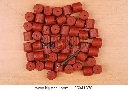 Fishing bait with hook and red pre-drilled halibut pellets for carp fishing isolated on wood background with soft shadow