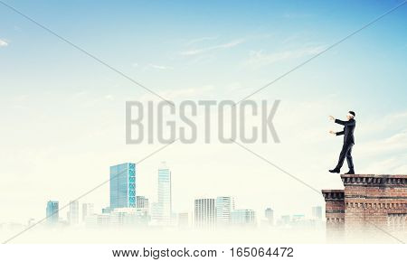 Businessman with blindfolder on eyes walking on building top