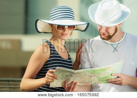 Summer travel concept. Young tourist couple on vacation sitting on city bench looking up directions on map