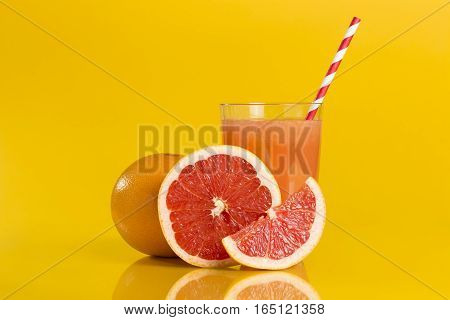 Whole red grapefruit cross section and a slice placed next to a glass of grapefruit juice with drinking straw isolated on orange background. Focus stacked image