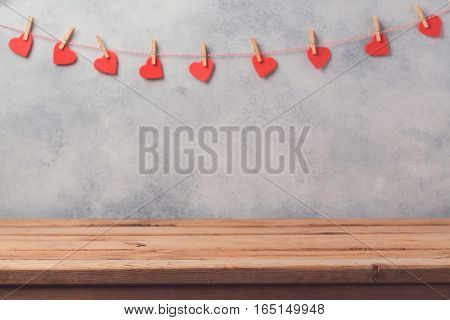 Empty wooden deck table over rustic wall background with heart shape garland. Valentines day concept