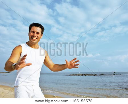 young brunette man on beach at sea smiling, gomosexual in white dress big muscles