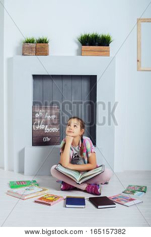 The child thinks schoolgirl sitting and reading a book. The concept of childhood training and education.