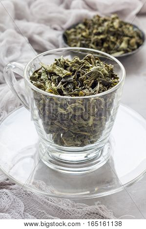 Dry green tea leaves in glass cup and on background vertical