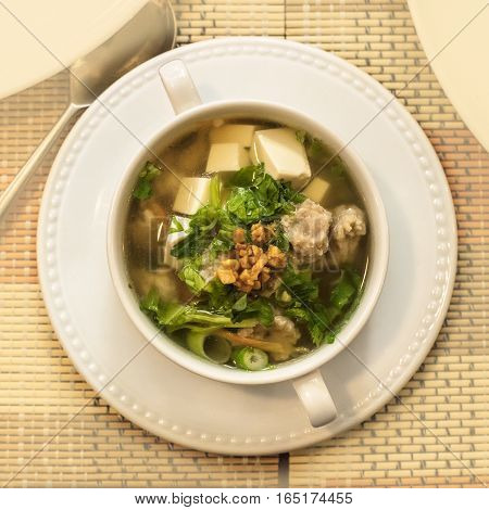 An overhead photo of a Thai soup with meatballs, vegetables, tofu, and soy noodles