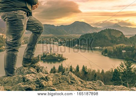 Man climbed on rocks at sunrise - Image with the legs of a tourist man climbed on rocks above the lake Bled in Slovenia looking at the beautiful sunrise and the Julian Alps