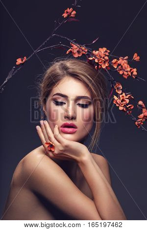 Beautiful young woman with make-up and loose hairdo holding artificial sakura branch with orange flowers. Beauty shot on dark background. Copy space.