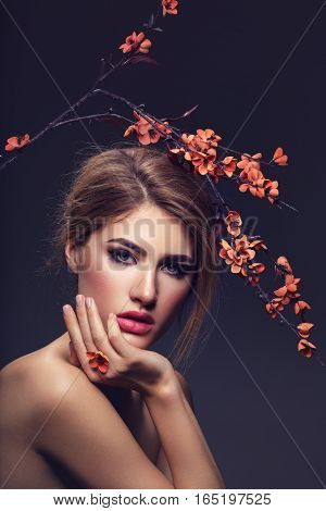 Beautiful young woman with make-up and loose hairdo holding artificial sakura branch with orange flowers. Beauty shot on dark background. Copy space.