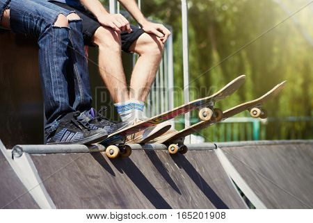 Couple of teenagers with boards sitting on top of mini-ramp in a skatepark ready to roll-in and do tricks