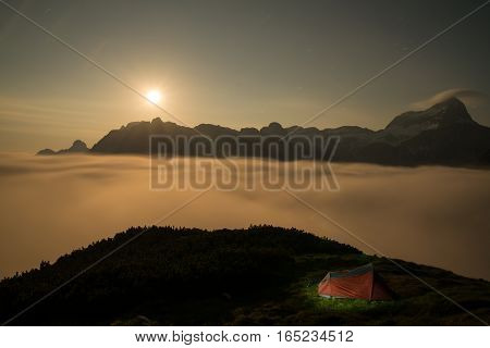 Illuminated red tent during summer night in mountains with moon
