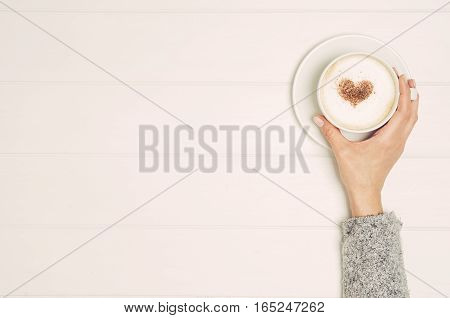 Female hand holding cup of coffee on white wooden table. Photograph taken from above, top view with copy space