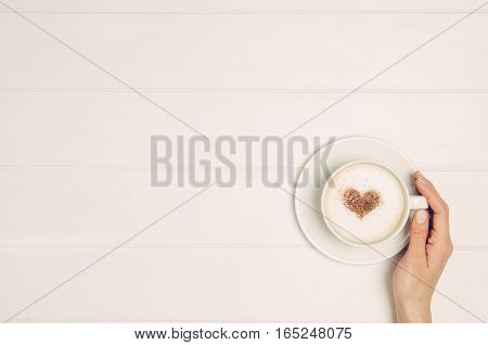 Female hand holding cup of coffee on white wooden table. Photograph taken from above, top view with copy space