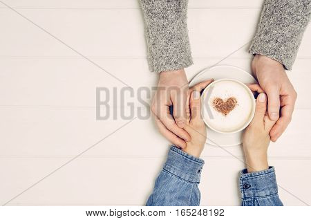 Couple in love holding hands with coffee on white wooden table. Photograph taken from above, top view with copy space