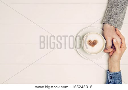 Couple in love holding hands with coffee on white wooden table. Photograph taken from above, top view with copy space