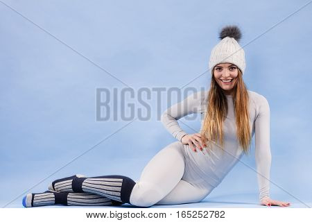 Fit woman in full length wearing winter cap gray sports thermal underwear warm socks studio shot on blue. Long sleeves top and leggings.
