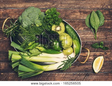 Retro styled food background. Raw detox green vegetable and herbs in old copper stew pot ready for cooking on rustic wooden background