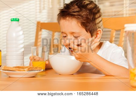 Close-up portrait of happy kid boy eating cereals with milk and drinking fresh orange juice